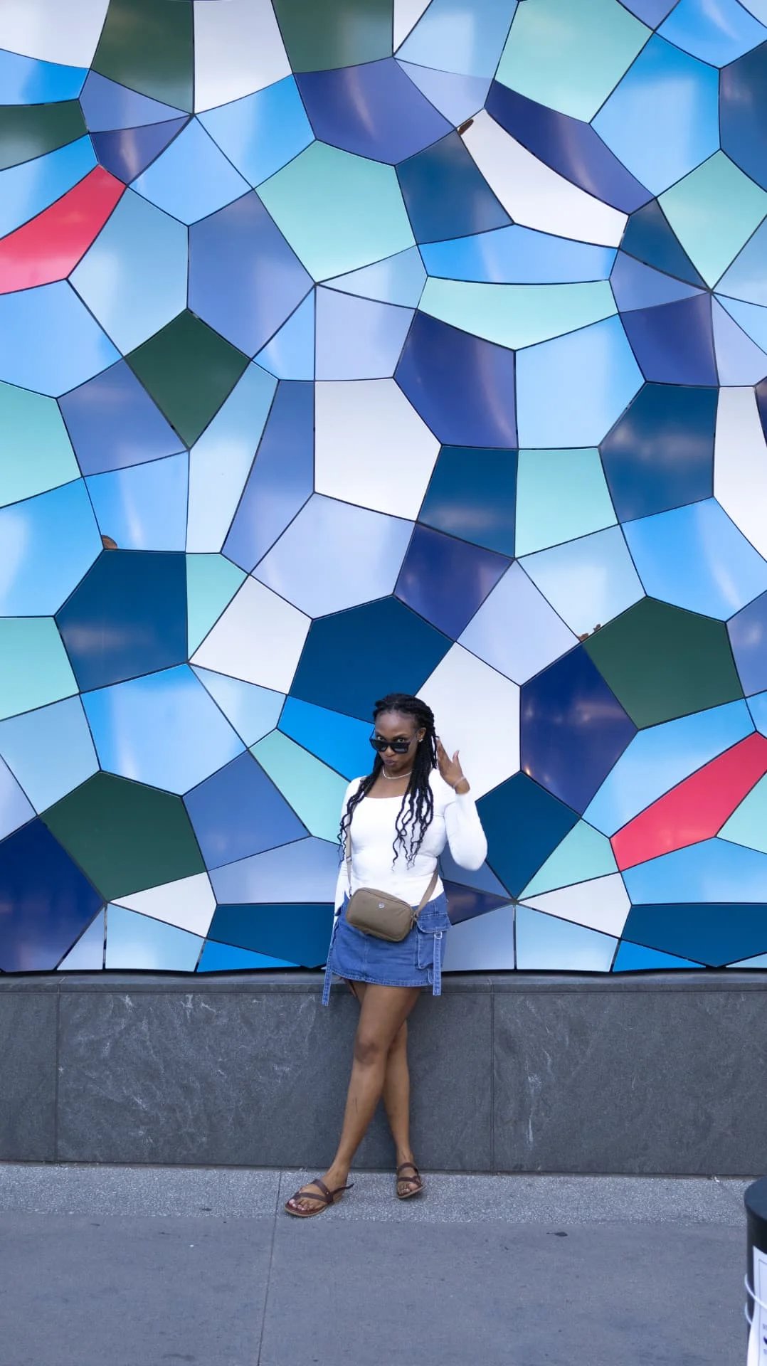 Woman in sunglasses posing against a blue geometric tiled wall