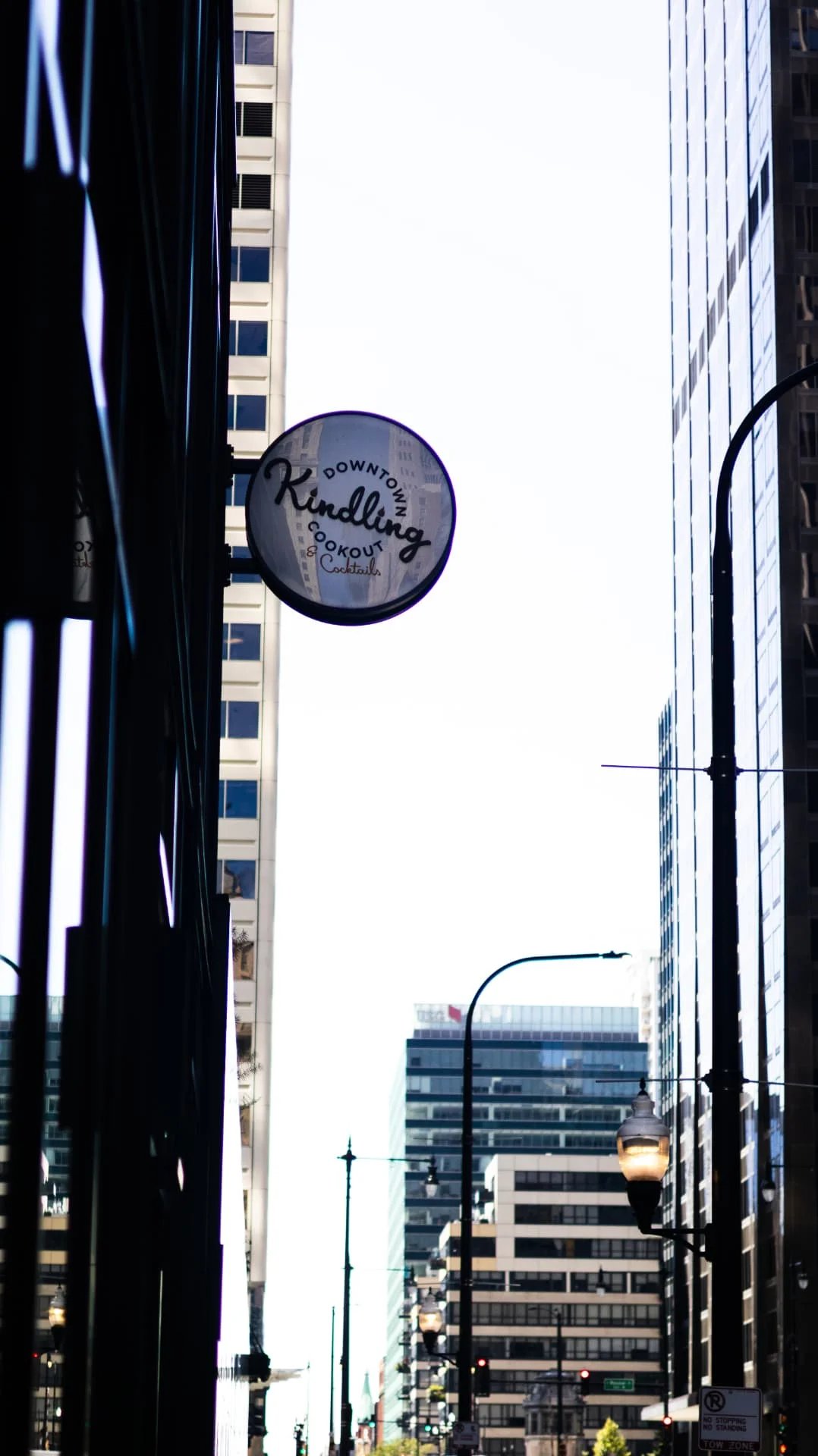 Round Kindling restaurant sign hanging between skyscrapers