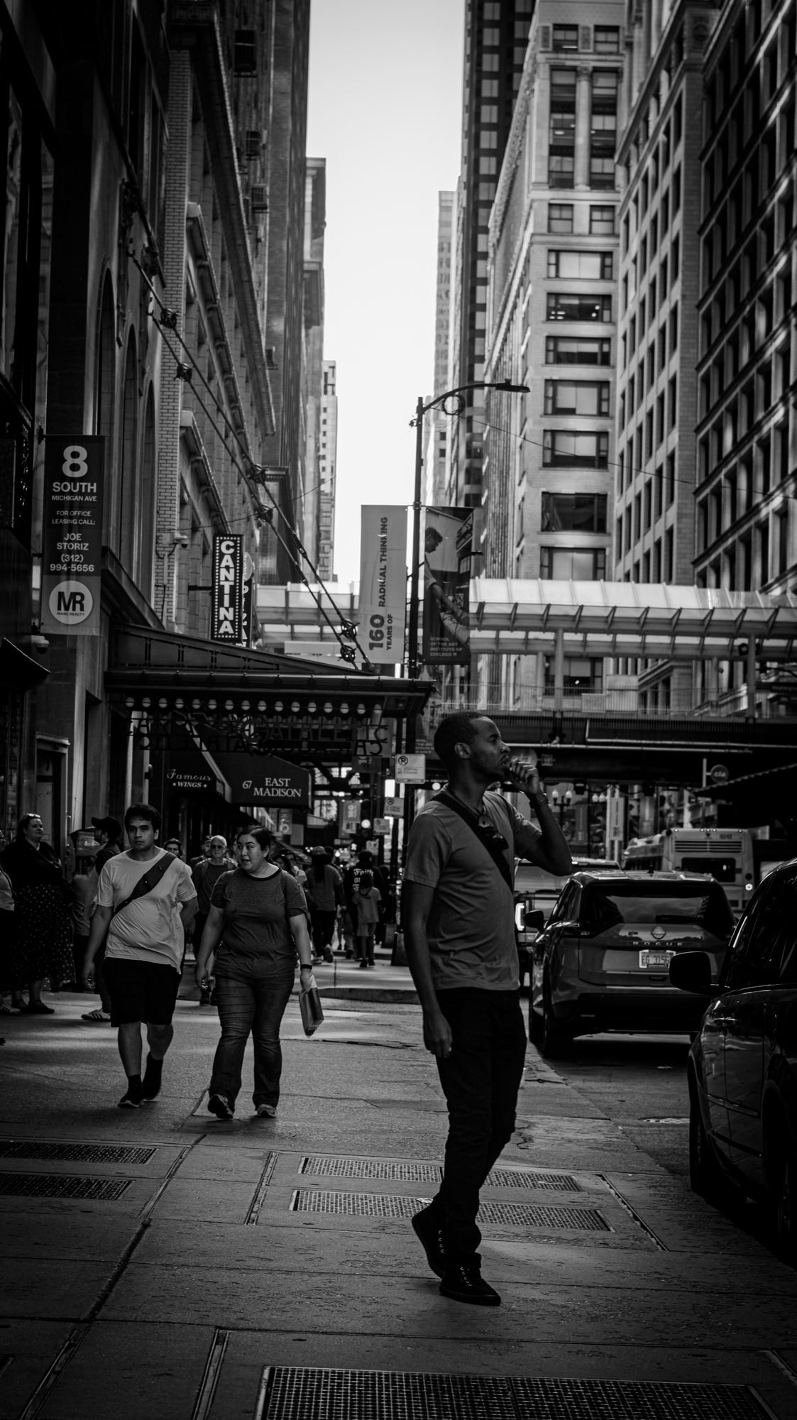 Black-and-white Chicago sidewalk, a man mid-stride under tall buildings and the elevated tracks