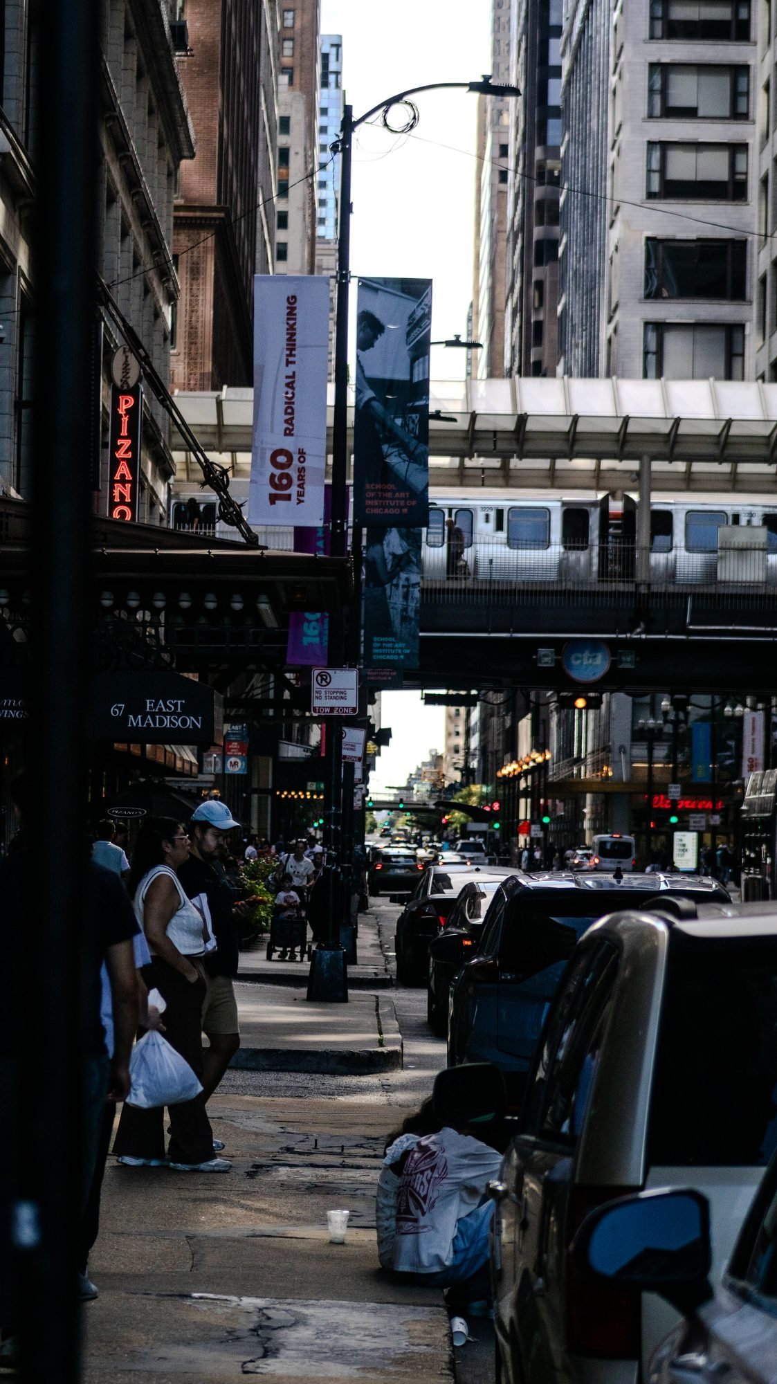 Loop street with art-school banners, a neon Pizano's sign and an L train crossing overhead