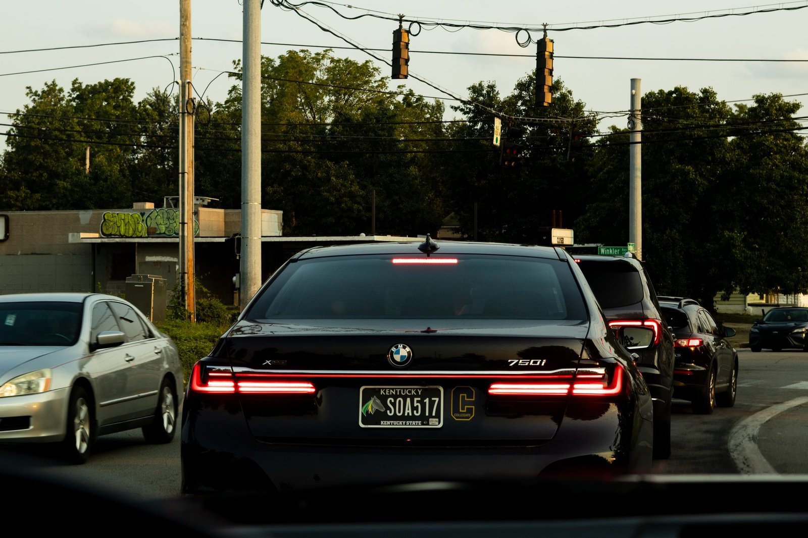 Black sedan's red tail lights glowing at a traffic signal at dusk