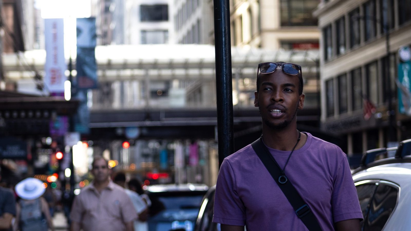 Man in a purple T-shirt with sunglasses on his head glancing sideways on a busy downtown street