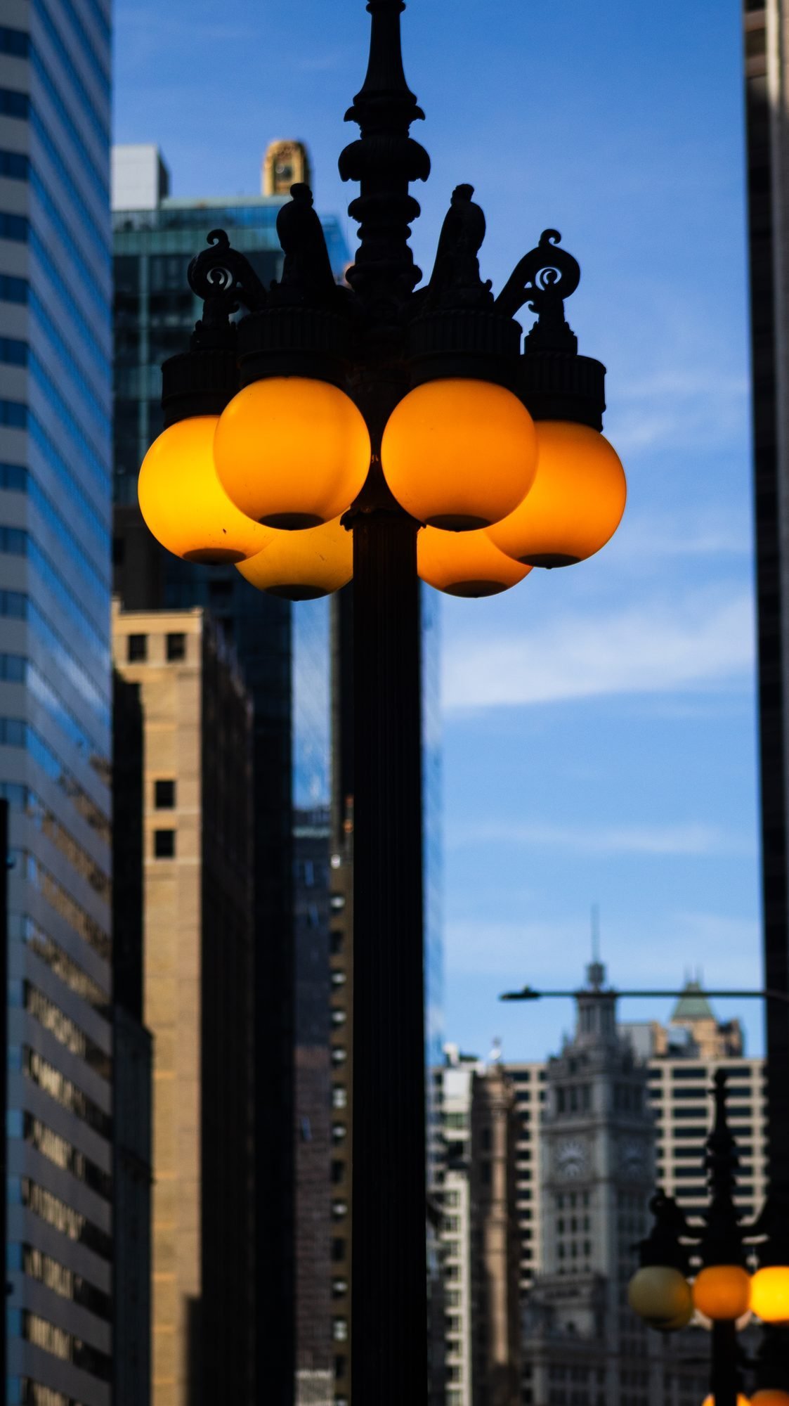 Ornate street lamp with glowing amber globes between towers under a blue sky