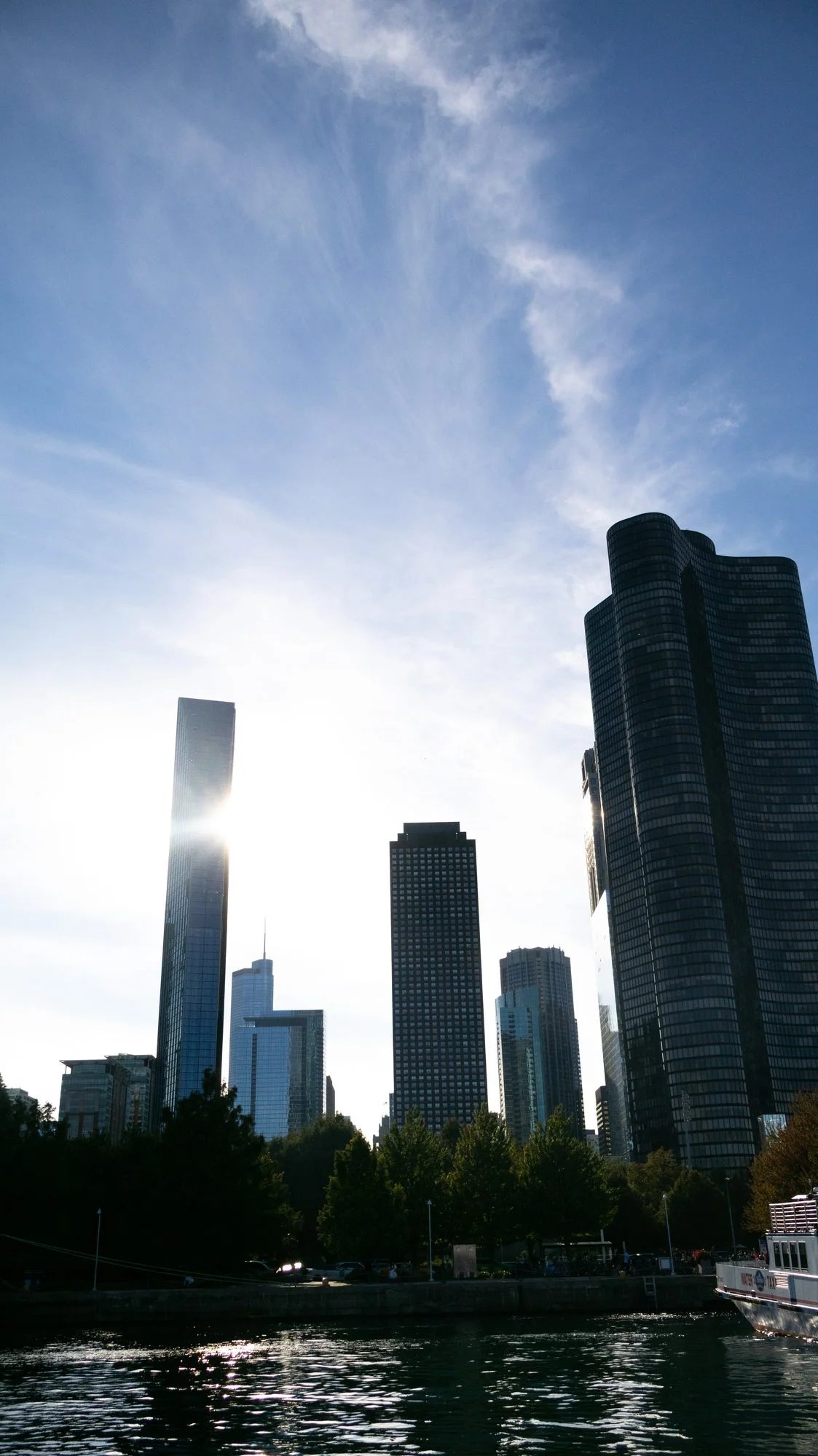 Chicago towers in silhouette with the sun flaring off a tall glass tower above the water