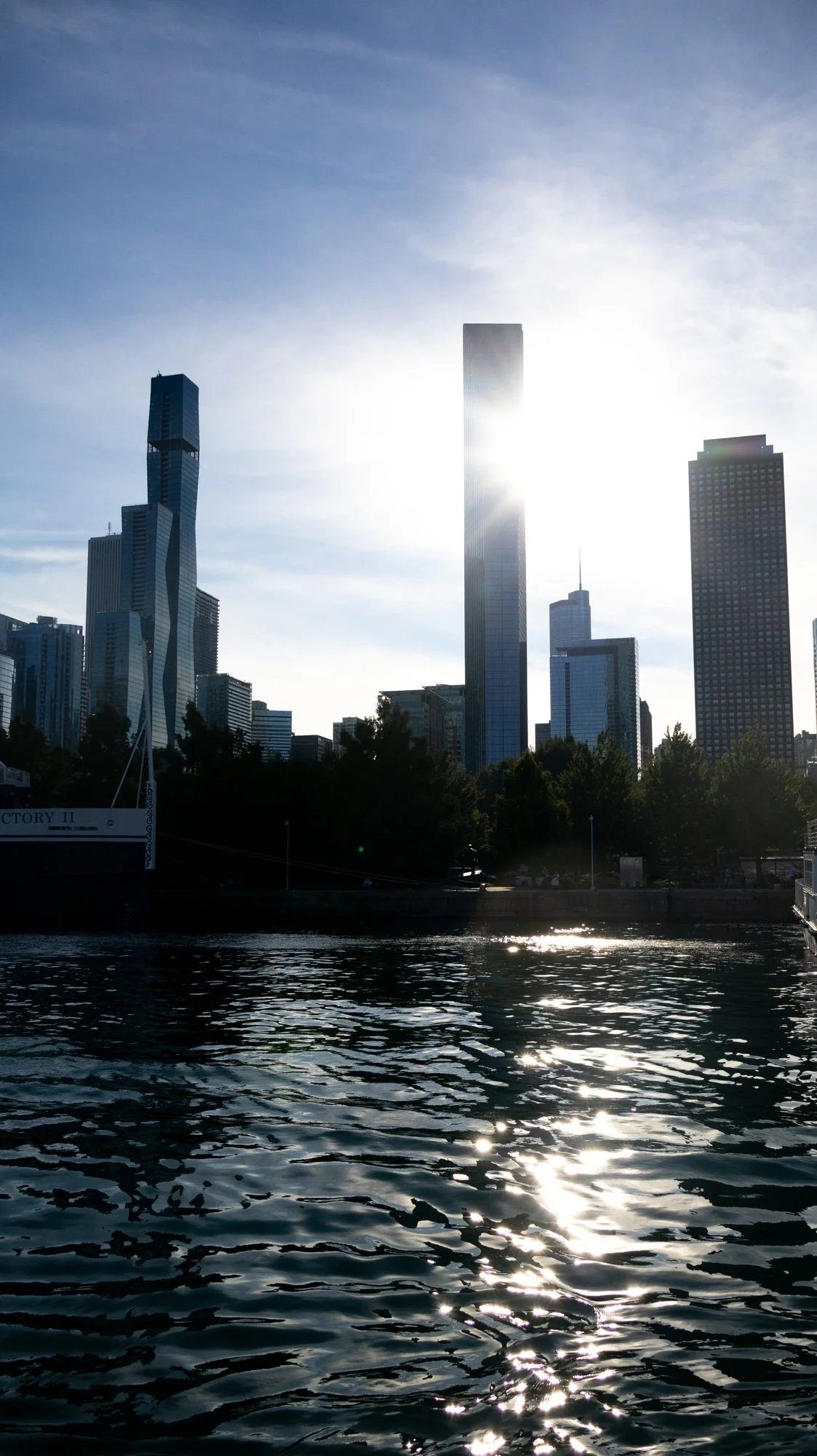 Sun burning through a slim skyscraper, light scattering across dark rippled water