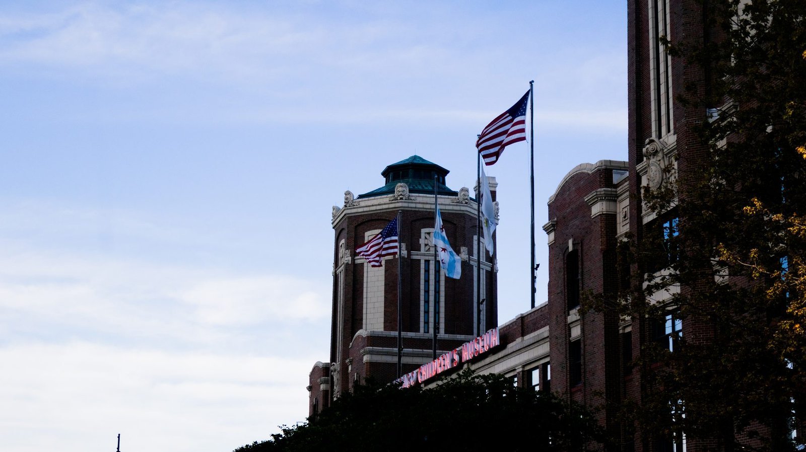 American and Chicago flags flying from a brick tower with a green copper roof